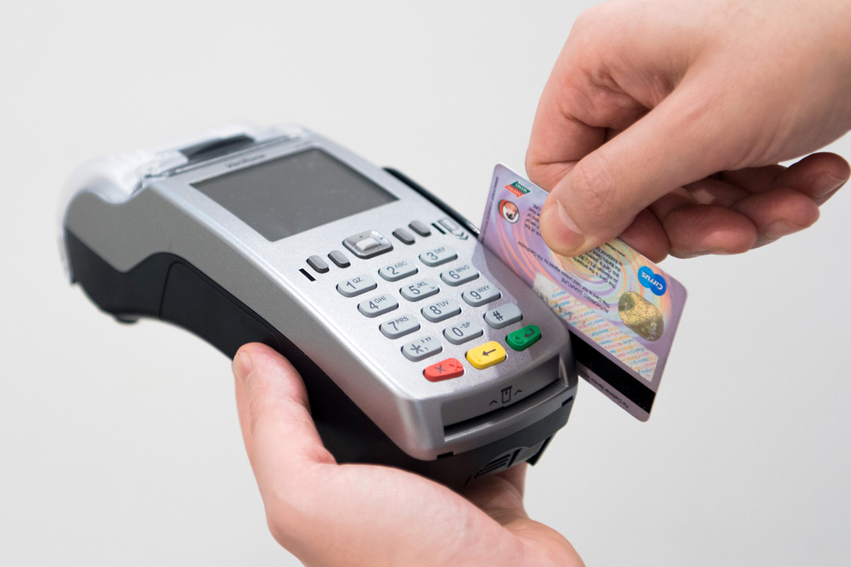 Due mani che reggono un POS e strisciano una carta di debito